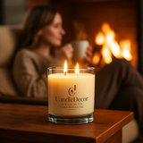 Candle with 'CandleDecor' branding in front of a person enjoying a cup of coffe by a fireplace