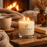 CandleDecor soy candle with a cup of coffee and decorative items on a wooden surface in front of a fireplace, showing a Danish Hygge atmosphere